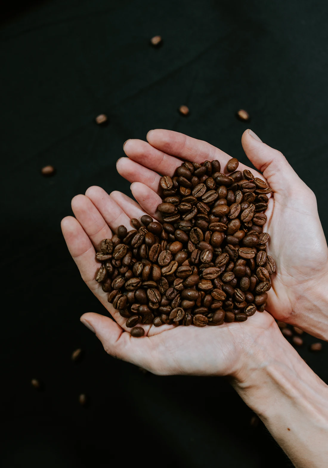 Manos sosteniendo granos de café tostado formando un corazón